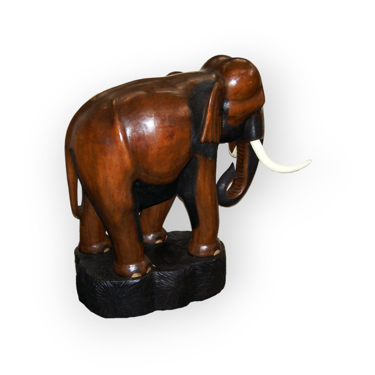 Carved wood elephant with white tusks, side view on dark base
