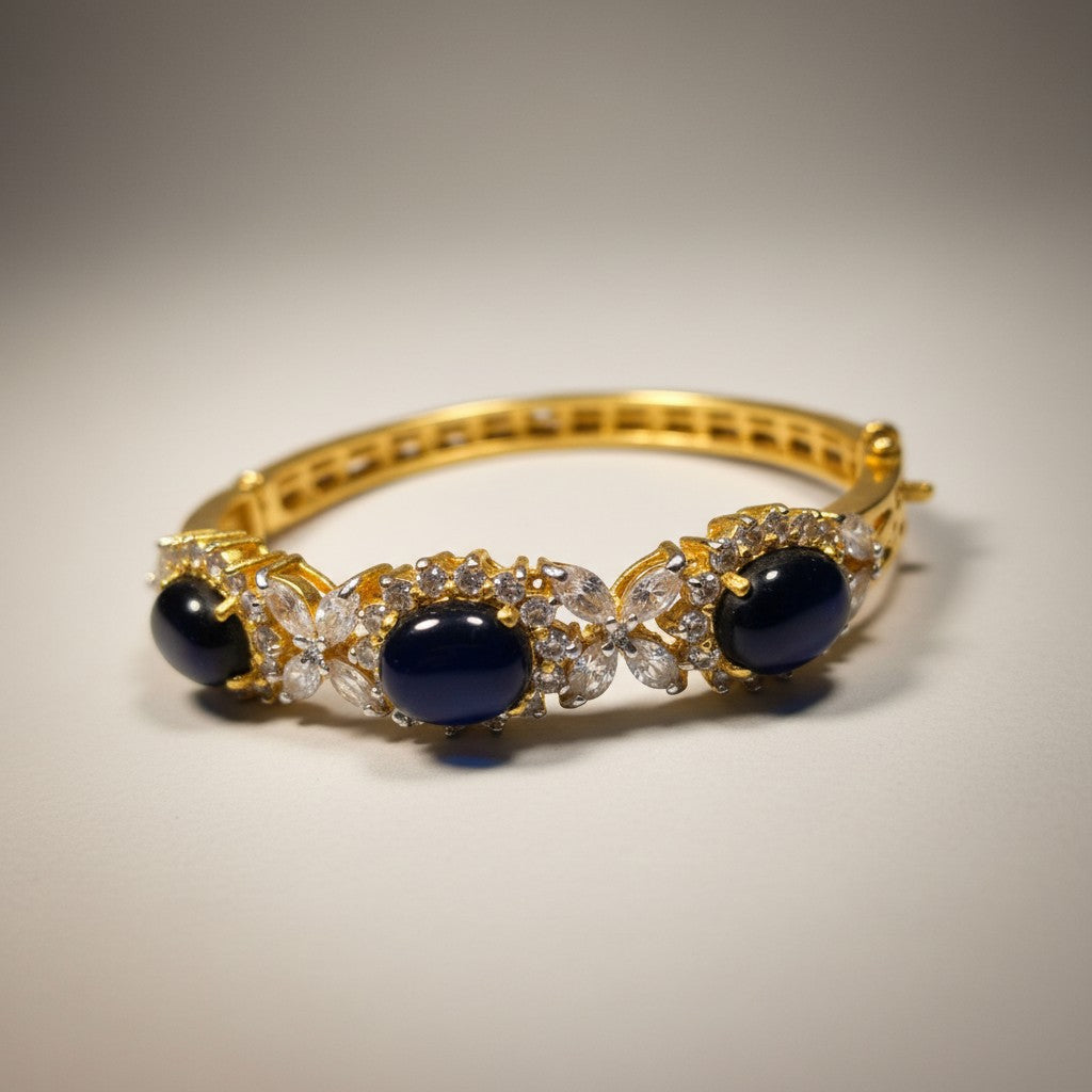 Dipped gold bangle with dark blue cabochon stones and clear stone accents, angled view