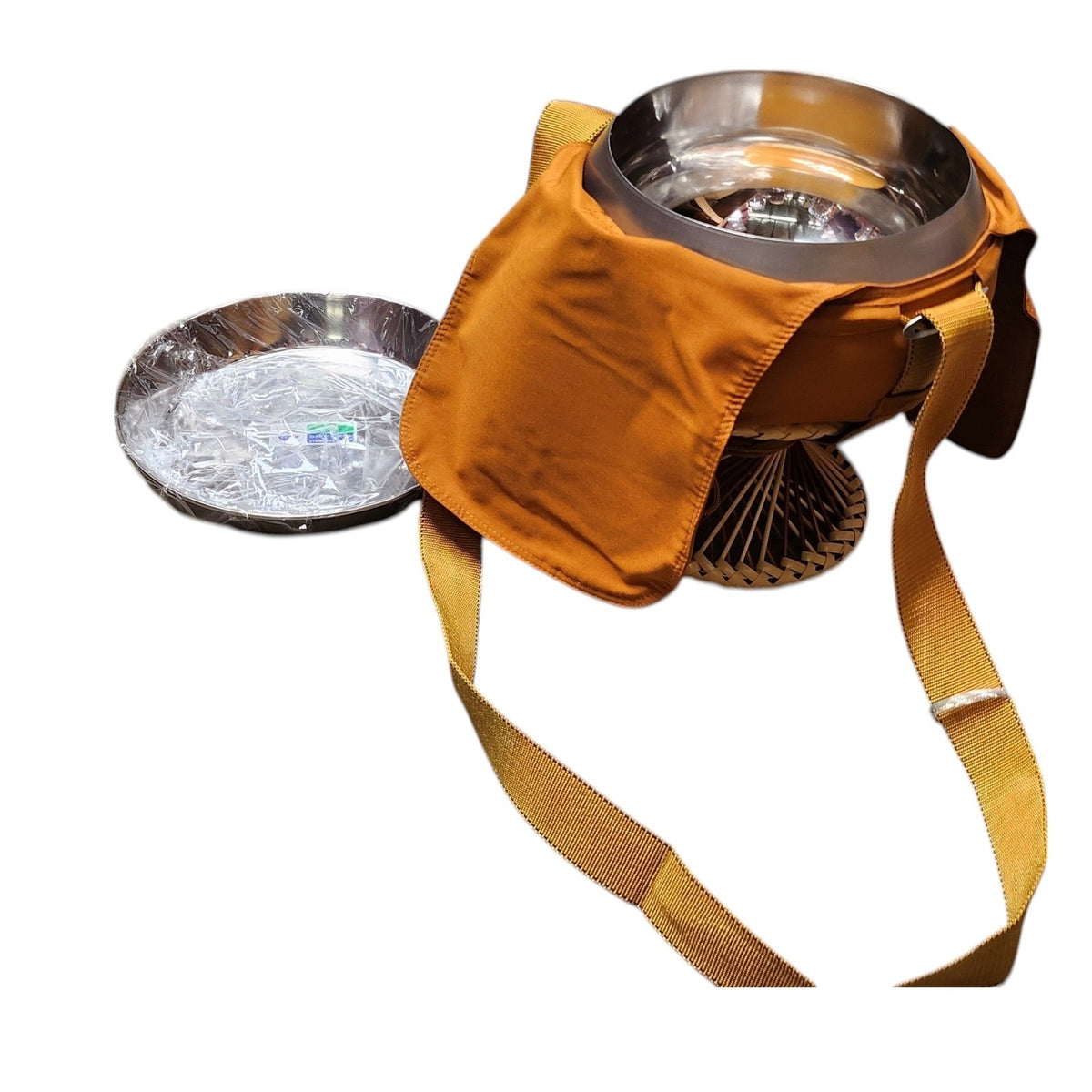 Alms bowl in orange cloth cover seen from above, with the steel plate leaning at left and the strap hanging down