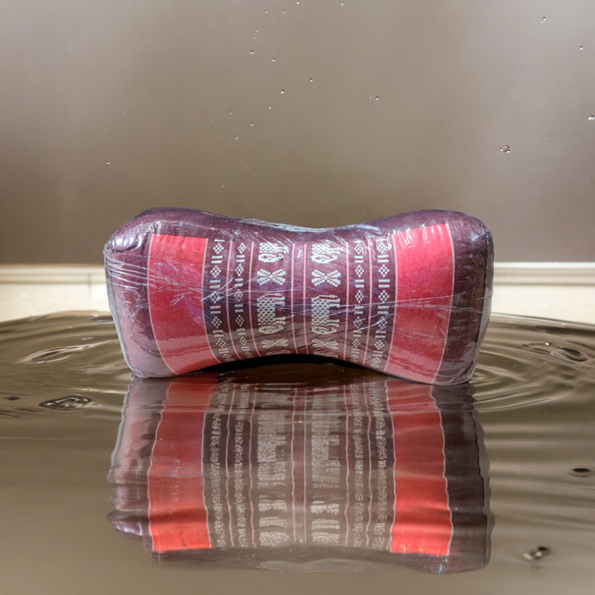 Bone-shaped kapok travel neck pillow in red and pink, shown on water