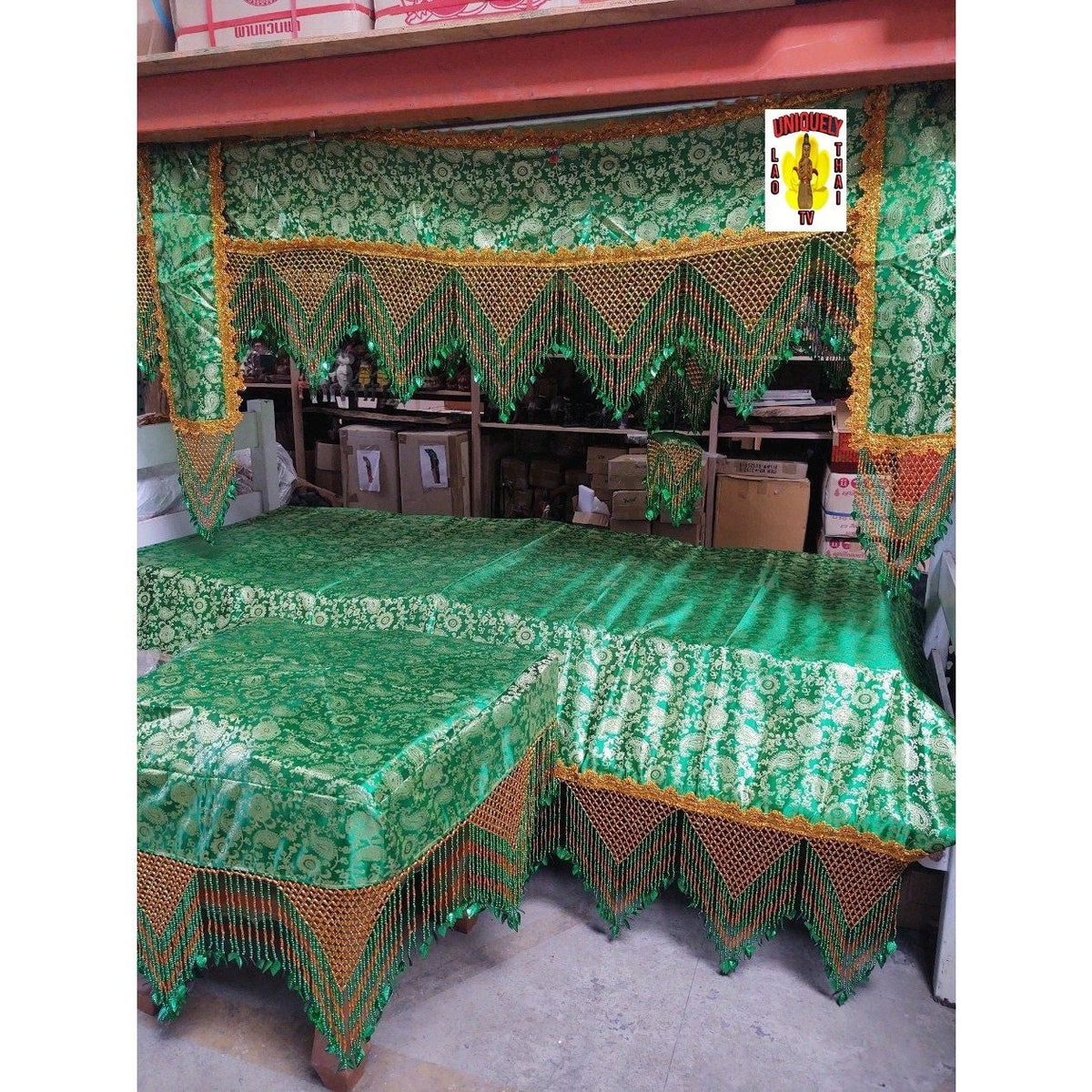 Red brocade funeral canopy with gold bead fringe, displayed over a bed