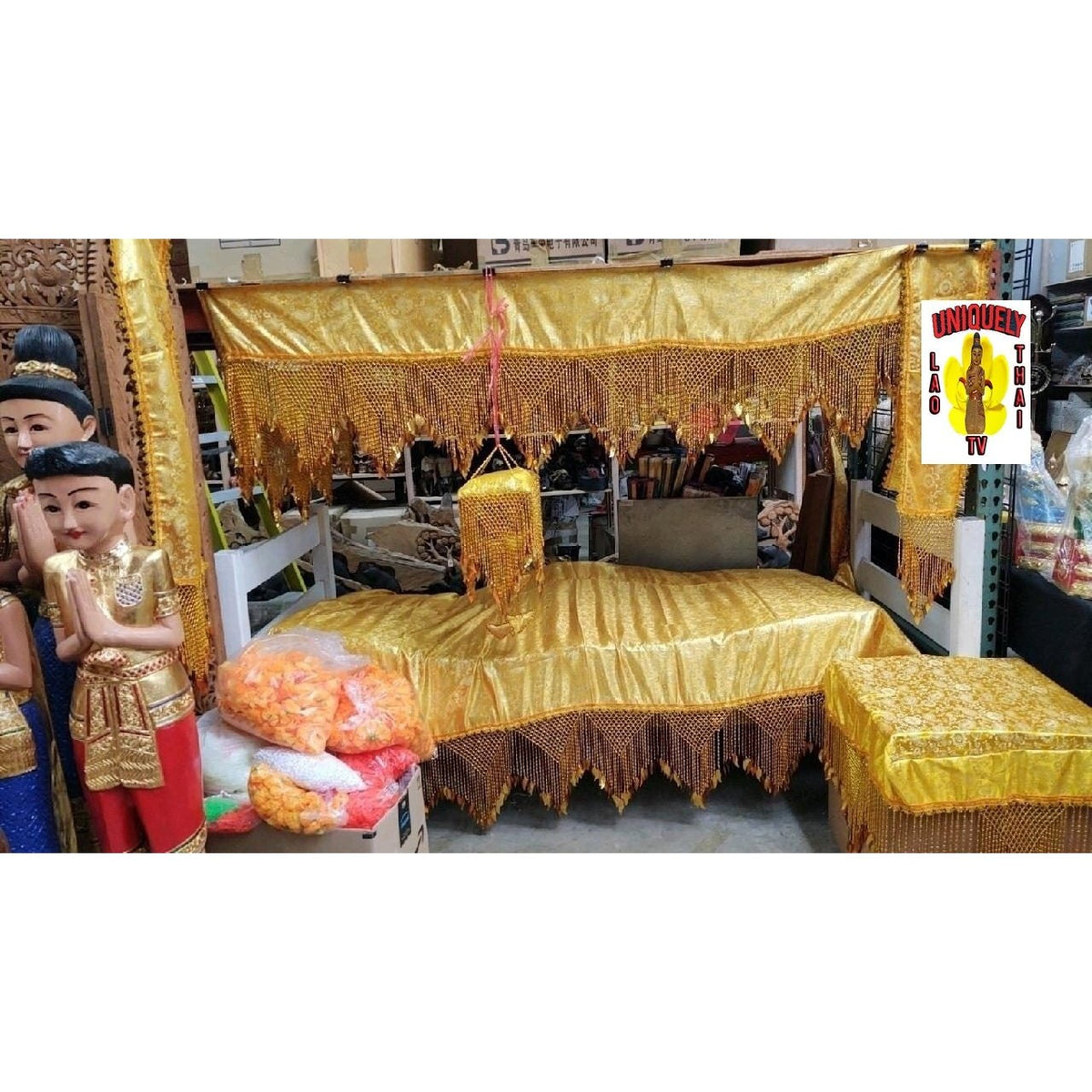 Red brocade funeral canopy with gold bead fringe, displayed over a bed