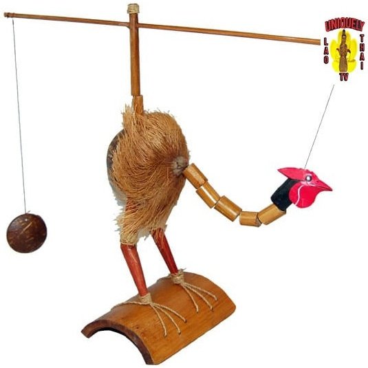 Coconut craft chicken with a red face standing on a curved roof tile beside a balancing pole and coconut weight